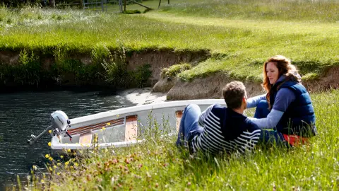 Twee personen zitten aan de oever naast een boot in het water.